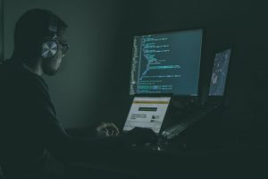 man wearing head set at desk with 2 monitors and a laptop