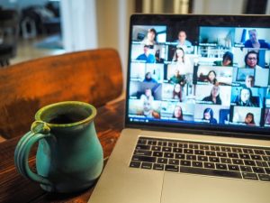MacBook laptop with multi-person video chat open. coffee mug on desk
