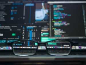 double monitor with code and pair of glasses on desk